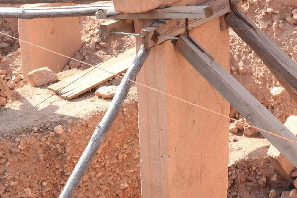 gobeklitepe (34) Kırmızı topraklı bir alanda, ahşap desteklerle güçlendirilmiş beton kolonlar ve kalaslar
