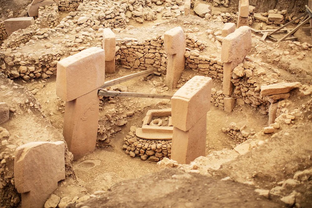 Arkeolojik kazı alanında, taş duvarlar arasında duran büyük T biçimli dikilitaşlar