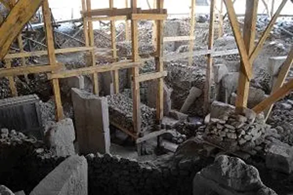 gobeklitepe (76) Ahşap iskeletli, taş duvarları ve molozları görünen kısmen yıkılmış bir yapı