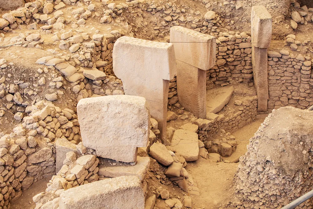 Arkeolojik kazı alanında toprağa gömülü büyük T biçimli taş sütunlar ve taş duvarlar