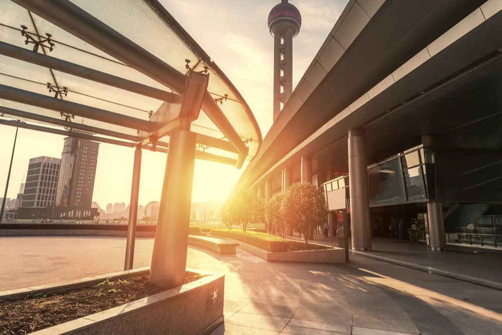 Gün batımında modern bir kent meydanı; yükseltilmiş yol ve küre tepeli kule görülüyor