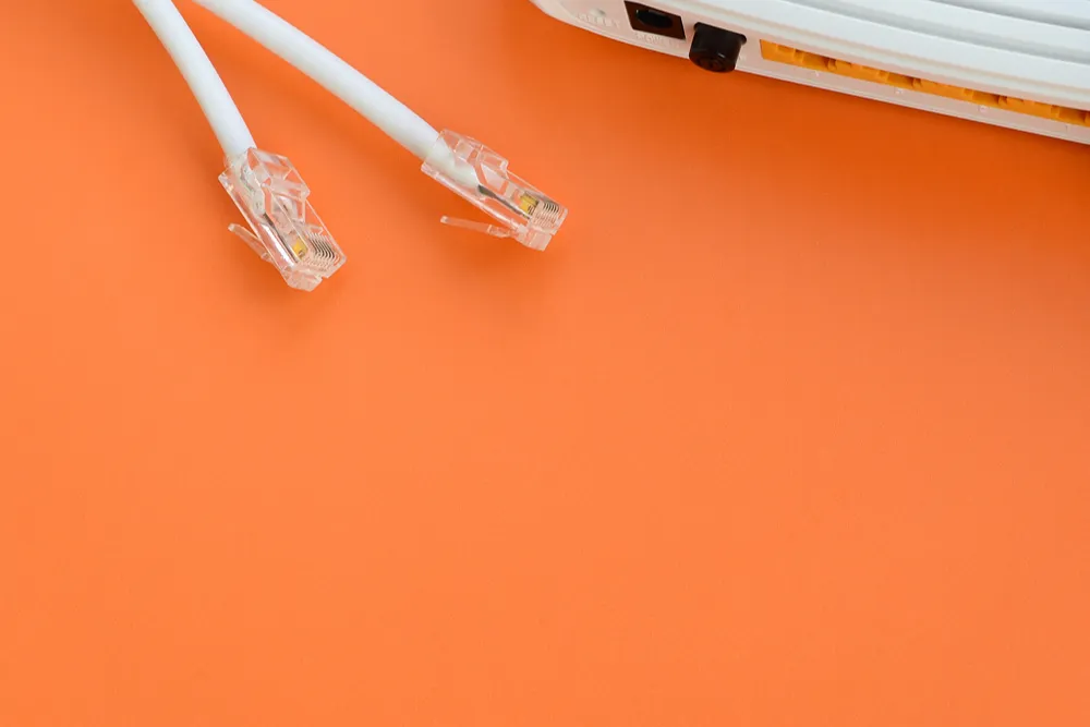Turuncu zemin üzerinde iki Ethernet kablosu ve kısmen görünen bir modem