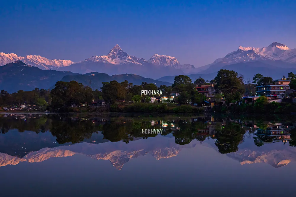 Pokhara'da göle yansıyan dağlar, ağaçlar ve şehir manzarası gün batımında görüntüleniyor